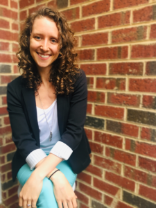 Image of Rosemary Bocian wearing a black blazer with a white shirt sitting up against a red brick wall smiling at the camera. 